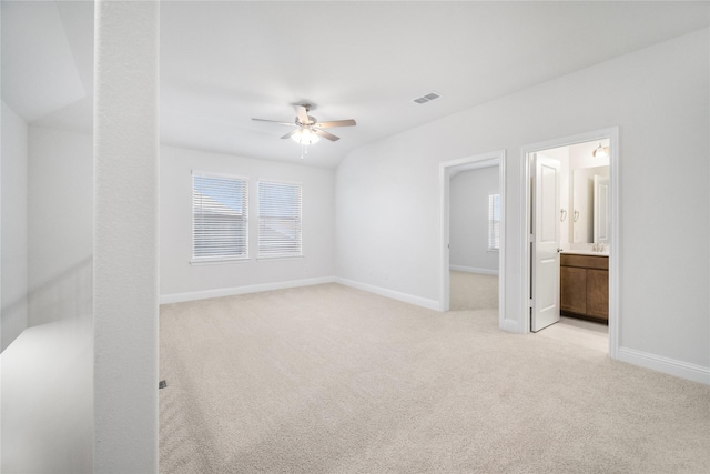 unfurnished bedroom featuring multiple windows, ensuite bathroom, light colored carpet, and ceiling fan