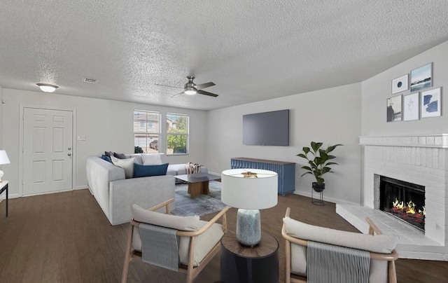 living room with a fireplace, ceiling fan, dark wood-type flooring, and a textured ceiling