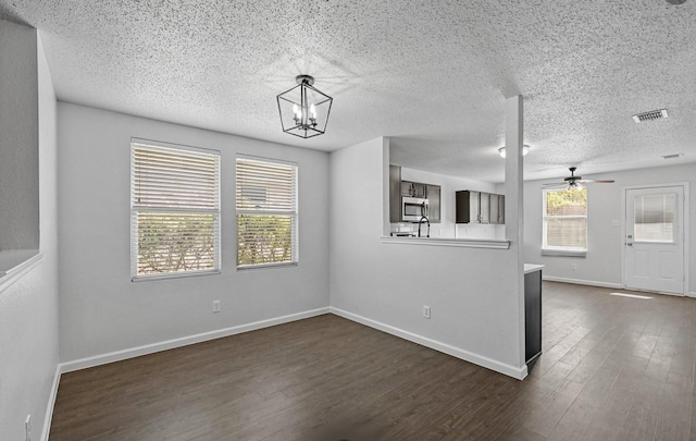 interior space with visible vents, dark wood-type flooring, baseboards, ceiling fan with notable chandelier, and a textured ceiling