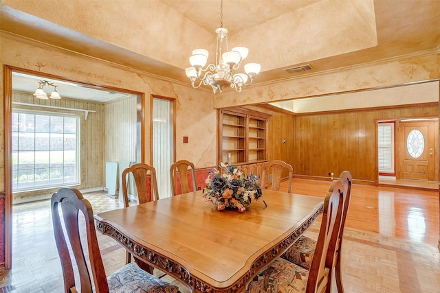 dining room featuring a tray ceiling, wood walls, a chandelier, and light parquet floors