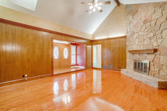 unfurnished living room featuring high vaulted ceiling, a stone fireplace, beam ceiling, hardwood / wood-style flooring, and wooden walls