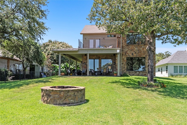 back of house featuring a balcony, an outdoor fire pit, and a lawn