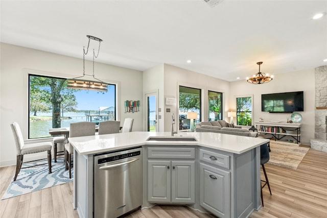 kitchen featuring light wood-type flooring, plenty of natural light, stainless steel dishwasher, and an island with sink