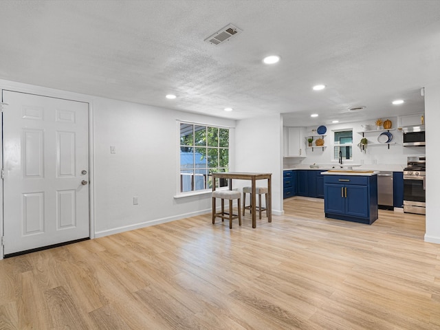 kitchen featuring a textured ceiling, stainless steel appliances, sink, blue cabinetry, and light hardwood / wood-style floors