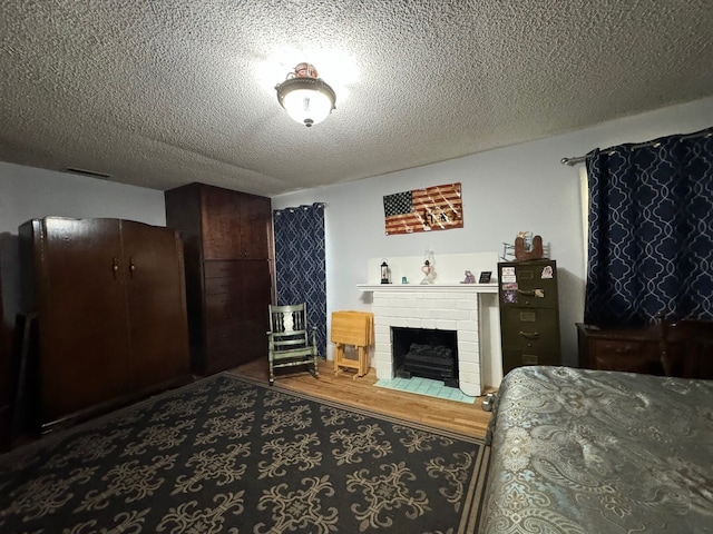 bedroom featuring hardwood / wood-style floors, a textured ceiling, and a brick fireplace