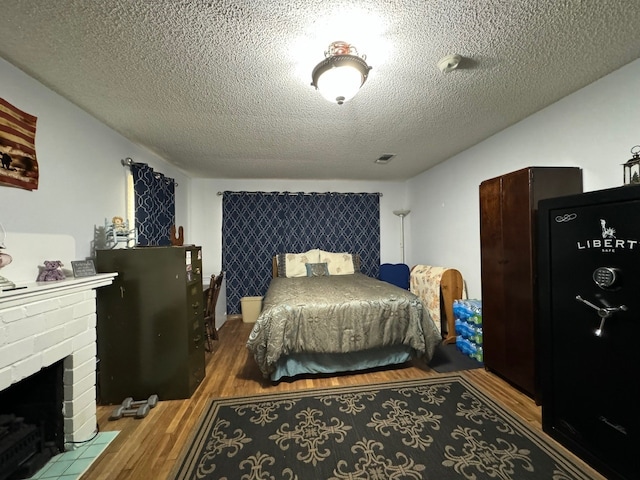 bedroom featuring a textured ceiling, hardwood / wood-style floors, and a brick fireplace