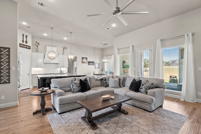 living room featuring ceiling fan with notable chandelier, sink, and light hardwood / wood-style flooring