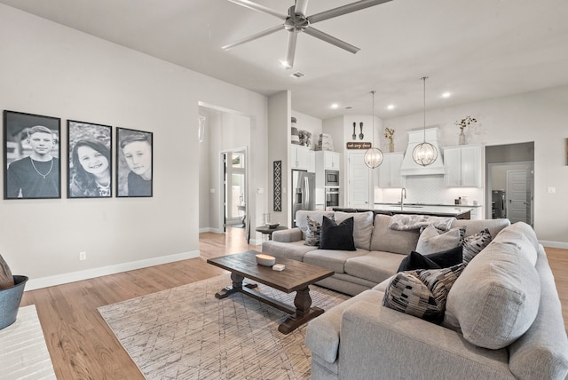 living room featuring ceiling fan, light wood-type flooring, and sink