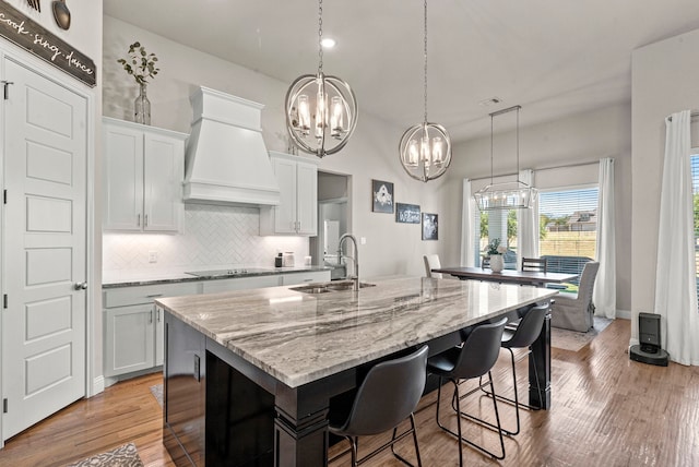 kitchen with backsplash, ventilation hood, sink, an island with sink, and light wood-type flooring