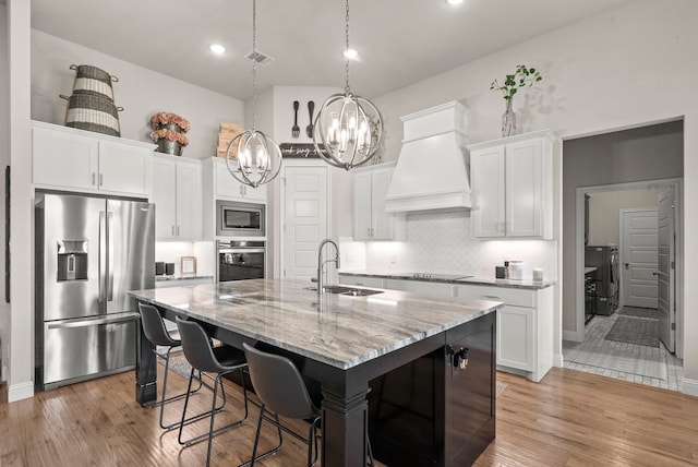 kitchen with sink, light wood-type flooring, appliances with stainless steel finishes, decorative backsplash, and premium range hood