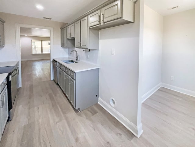 kitchen with sink, light hardwood / wood-style floors, stainless steel dishwasher, and gray cabinets