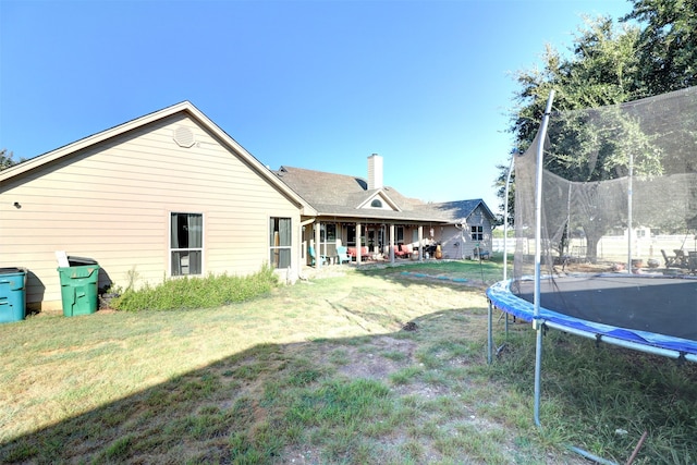 back of property featuring a trampoline and a lawn