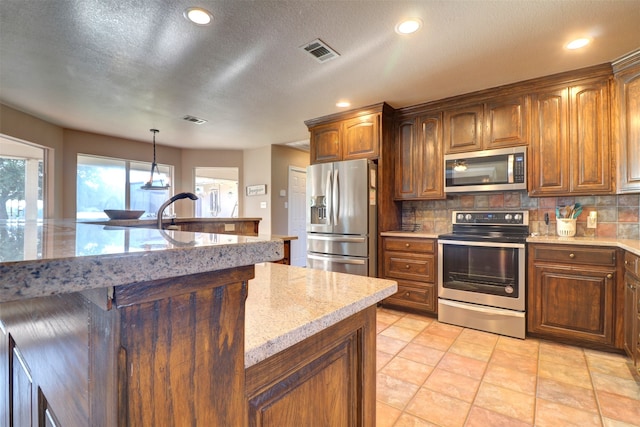 kitchen with tasteful backsplash, stainless steel appliances, light stone countertops, hanging light fixtures, and light tile patterned floors