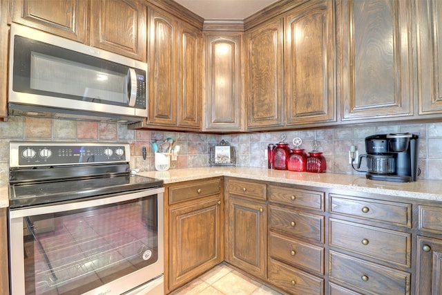 kitchen featuring appliances with stainless steel finishes, light stone counters, light tile patterned floors, and tasteful backsplash