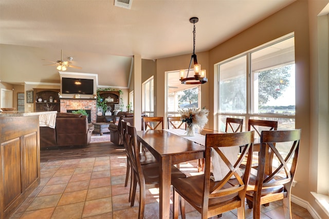 dining space featuring ceiling fan with notable chandelier, a brick fireplace, lofted ceiling, and tile patterned flooring