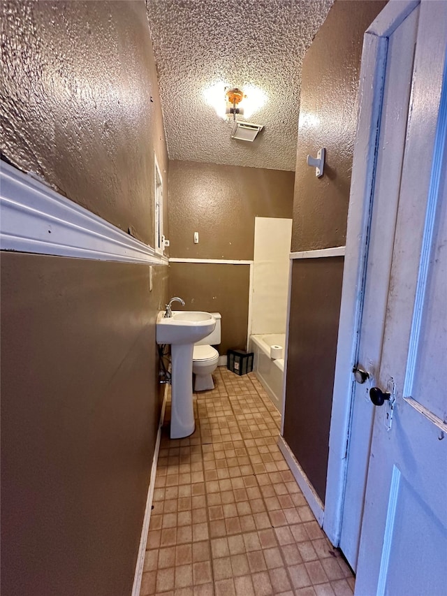 bathroom featuring a textured ceiling, toilet, and a tub