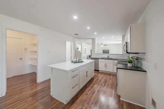 kitchen with appliances with stainless steel finishes, a center island, white cabinetry, and dark wood-type flooring