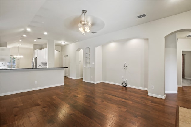 unfurnished living room featuring ceiling fan with notable chandelier and dark hardwood / wood-style flooring