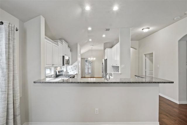 kitchen featuring kitchen peninsula, dark stone counters, white cabinetry, appliances with stainless steel finishes, and dark hardwood / wood-style flooring