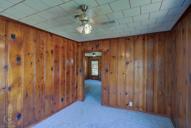 empty room featuring ceiling fan, wooden walls, and light carpet