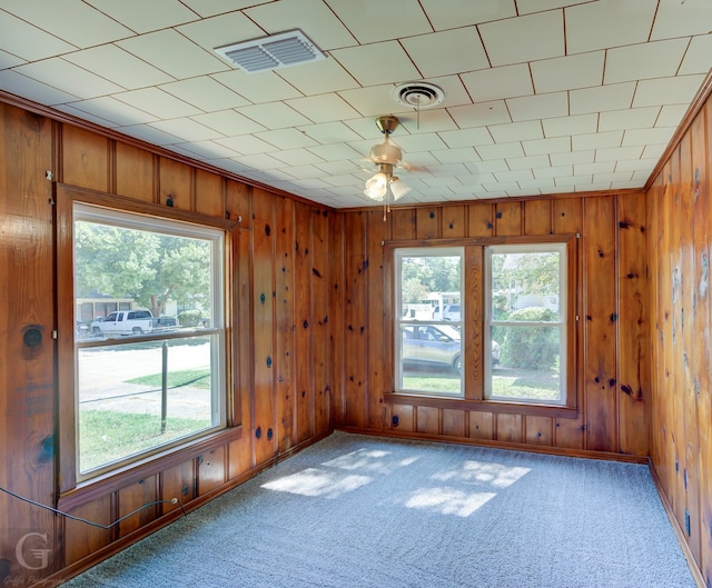 empty room featuring wood walls, ceiling fan, and light carpet