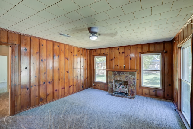 unfurnished living room with carpet floors, a fireplace, wood walls, and a healthy amount of sunlight