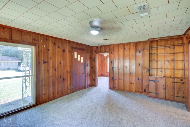 carpeted spare room featuring ceiling fan, a wealth of natural light, and wooden walls