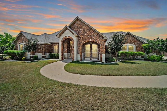 french country home with brick siding and a lawn