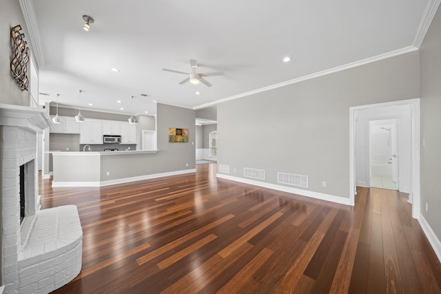 unfurnished living room featuring hardwood / wood-style floors, ceiling fan, crown molding, and a brick fireplace