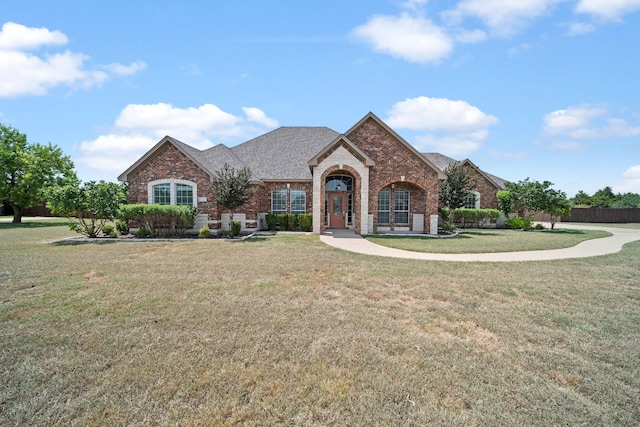 french provincial home featuring brick siding, a front lawn, and a shingled roof