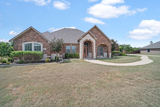 view of front of house featuring a shingled roof, a front yard, and brick siding