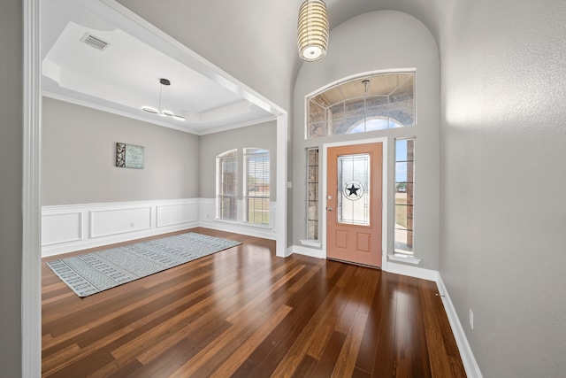 foyer with a tray ceiling, dark wood-type flooring, ornamental molding, and a high ceiling