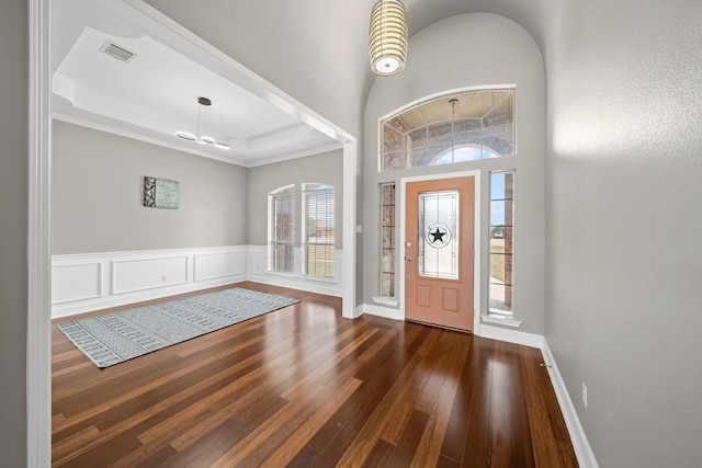 foyer featuring visible vents, wainscoting, ornamental molding, dark wood-style flooring, and a tray ceiling