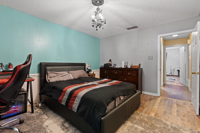 bedroom with an inviting chandelier, light hardwood / wood-style flooring, and a textured ceiling