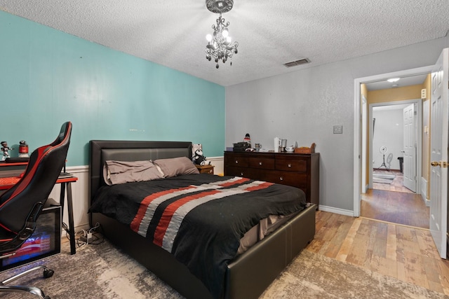 bedroom with an inviting chandelier, a textured ceiling, visible vents, and wood finished floors