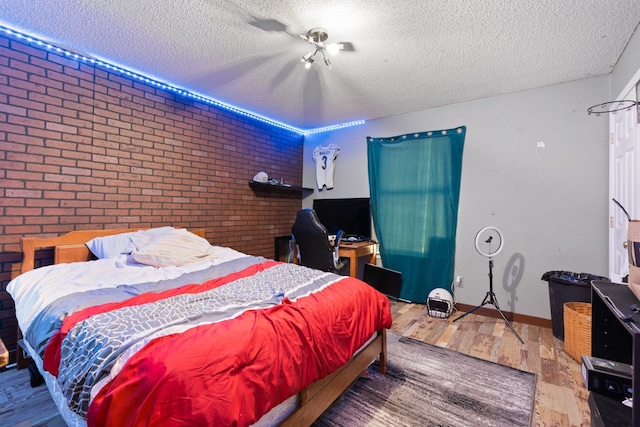 bedroom with hardwood / wood-style floors, brick wall, and a textured ceiling