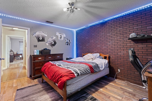 bedroom with wood-type flooring, brick wall, and a textured ceiling