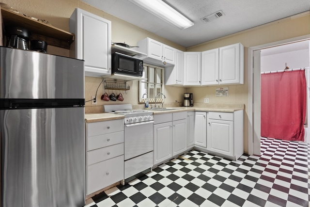 kitchen with stainless steel refrigerator, sink, white cabinets, light tile patterned floors, and white gas range