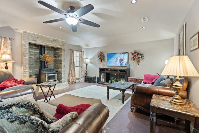 living room featuring ceiling fan, brick wall, a wood stove, and a fireplace