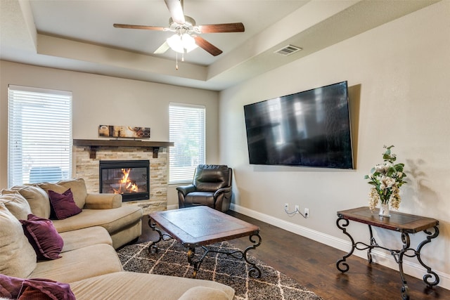 living room featuring visible vents, baseboards, wood finished floors, a tray ceiling, and a fireplace