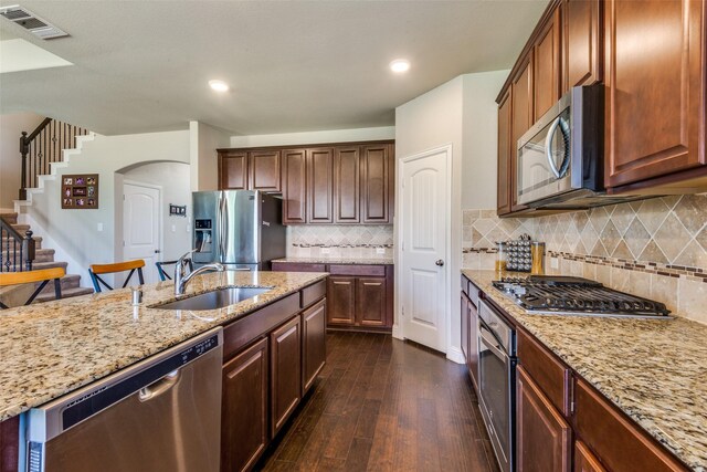 kitchen featuring arched walkways, dark wood-style flooring, stainless steel appliances, a sink, and light stone countertops