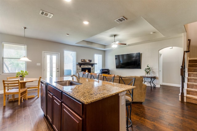 kitchen with a tray ceiling, visible vents, stainless steel dishwasher, a sink, and a stone fireplace