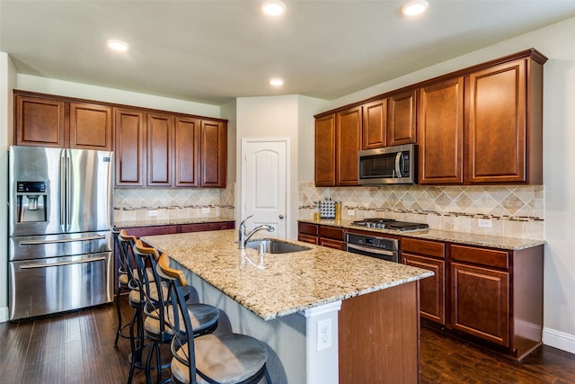 kitchen featuring a sink, appliances with stainless steel finishes, light stone counters, and dark wood-style flooring