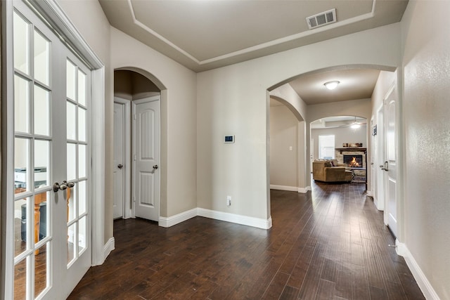 hallway with arched walkways, dark wood-style flooring, visible vents, and baseboards