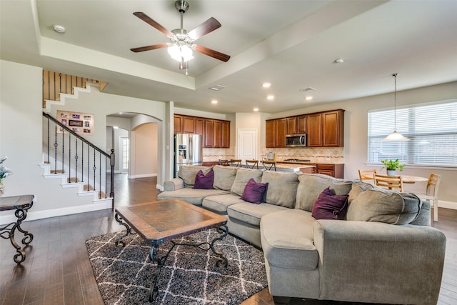 living room featuring arched walkways, dark wood finished floors, a raised ceiling, stairway, and baseboards