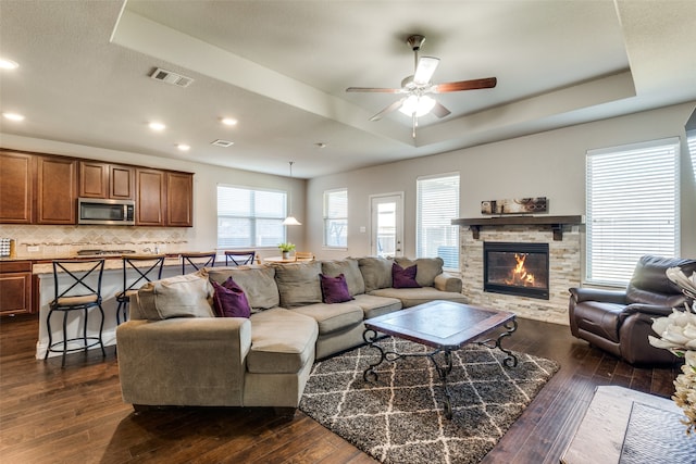 living room with a tray ceiling, dark wood-type flooring, and a fireplace