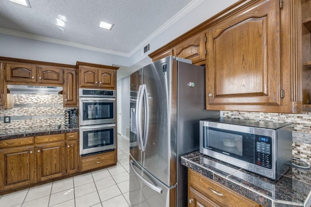 kitchen with tasteful backsplash, crown molding, a textured ceiling, light tile patterned floors, and appliances with stainless steel finishes