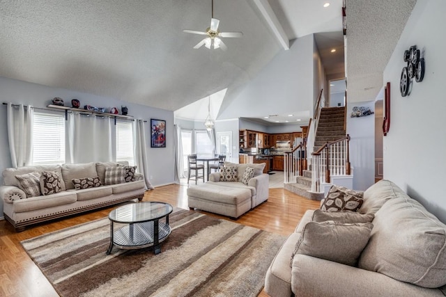 living room with high vaulted ceiling, light hardwood / wood-style flooring, ceiling fan, a textured ceiling, and beamed ceiling