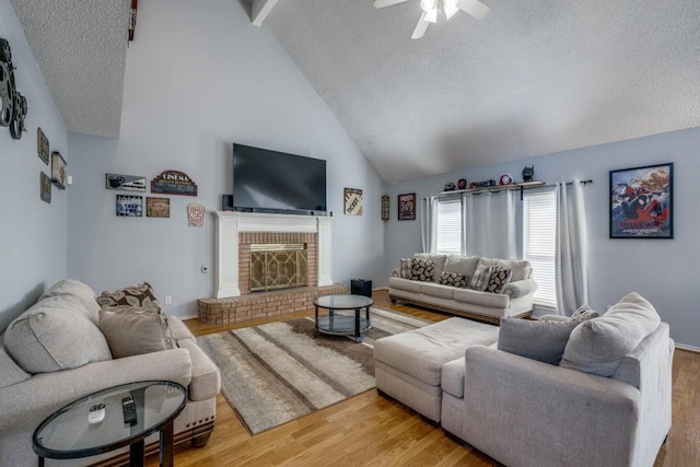 living room with a textured ceiling, ceiling fan, hardwood / wood-style flooring, high vaulted ceiling, and a fireplace