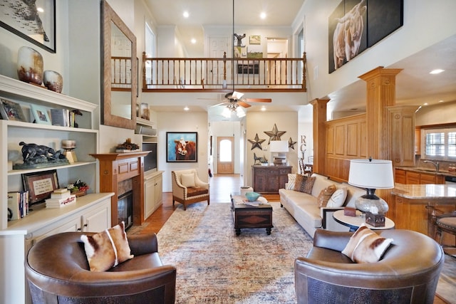 living room with ornate columns, sink, a high ceiling, ceiling fan, and light hardwood / wood-style floors